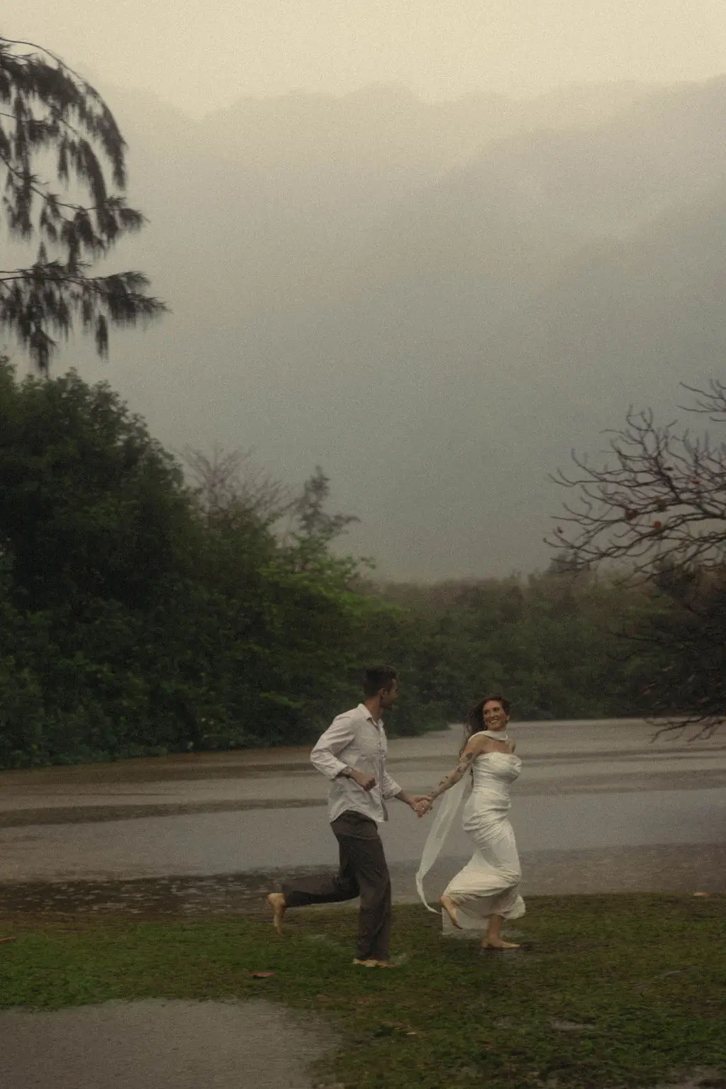 Bride and groom dance barefoot on grass before fog-wrapped mountains