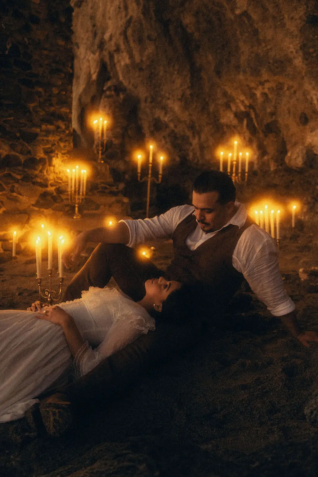 Bride reclines against groom surrounded by lit candles inside a rocky cave