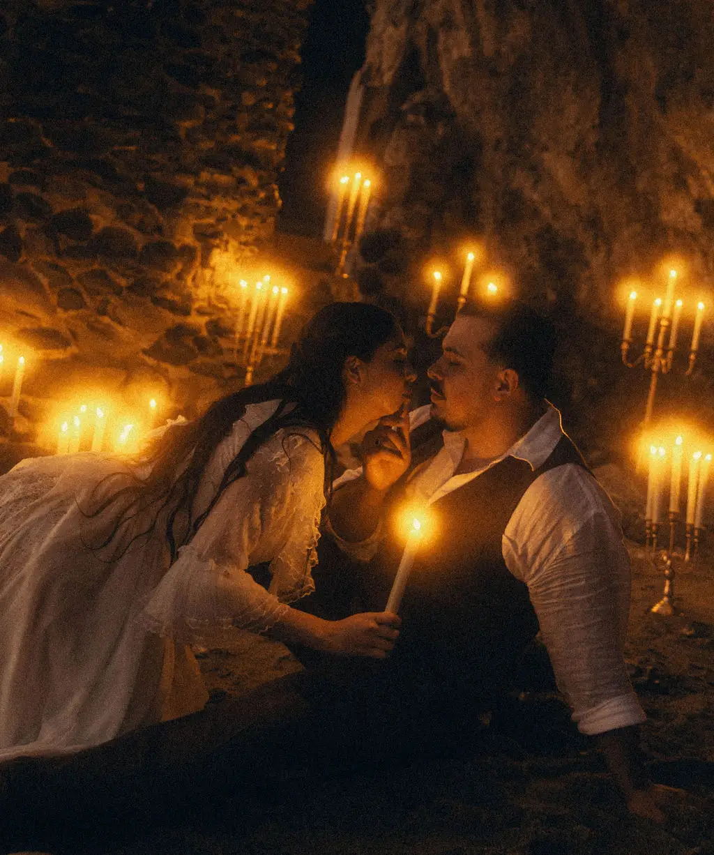 Bride and groom lean close holding a candle among many flames in a dim cave