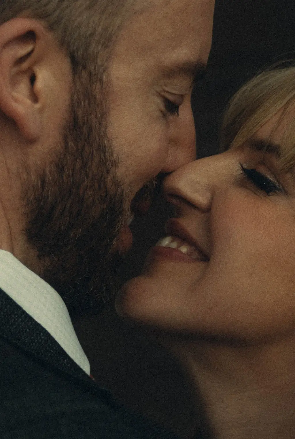 Close portrait of groom nuzzling smiling bride cheek to cheek in warm light
