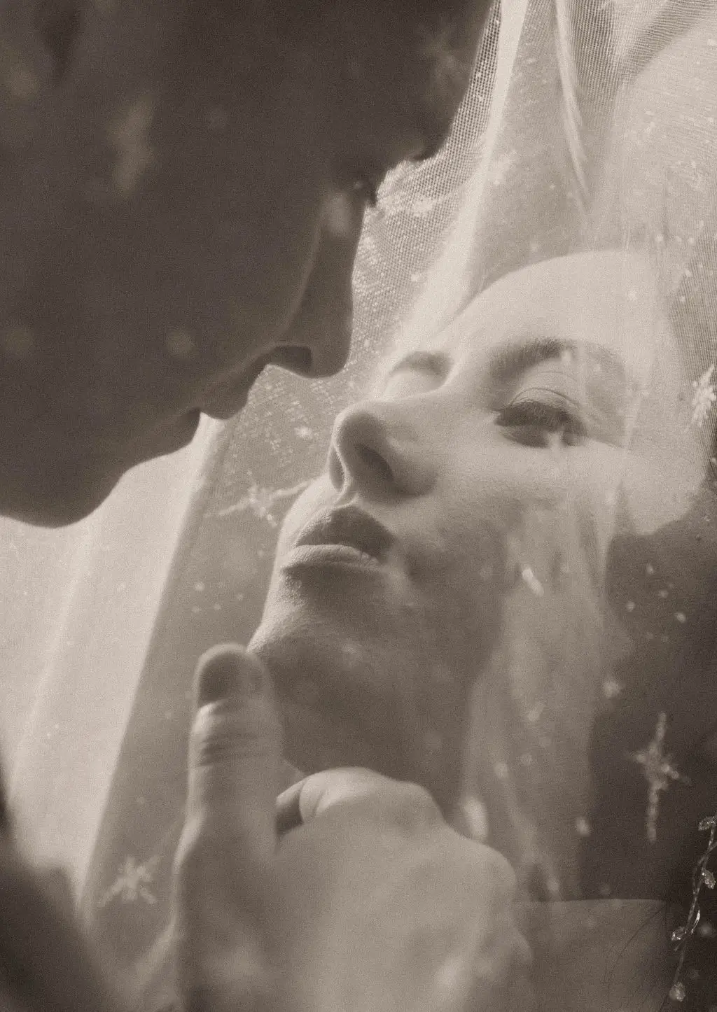 Sepia close portrait of bride and groom about to kiss beneath a sheer starry veil