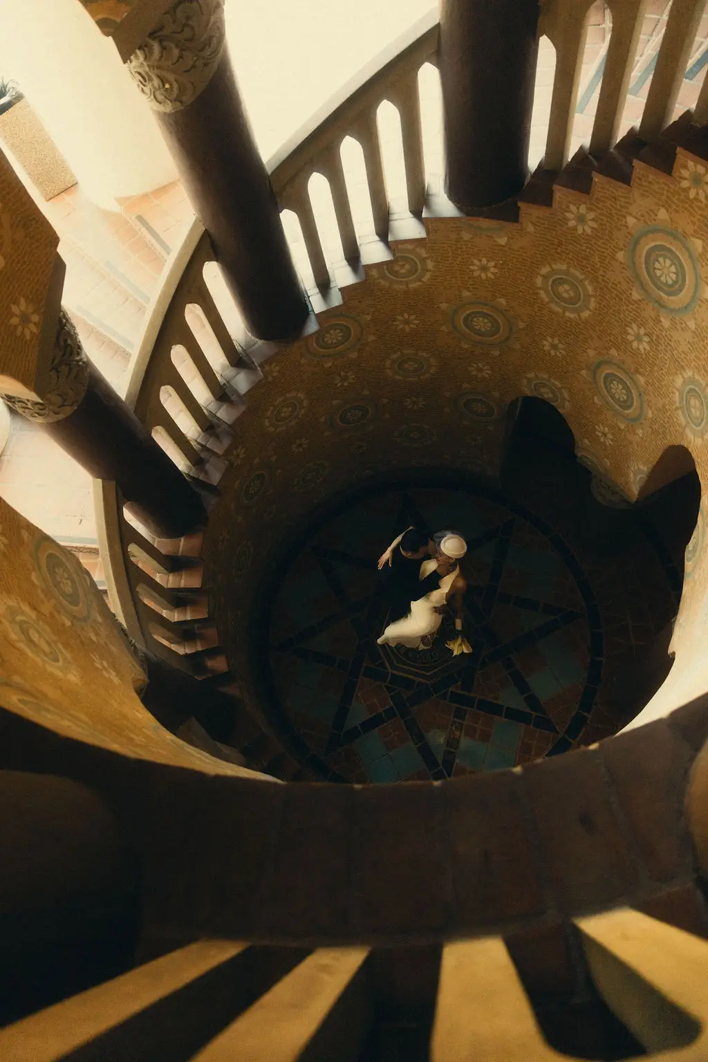Overhead view of bride and groom embracing on a star-tiled floor within an ornate spiral staircase