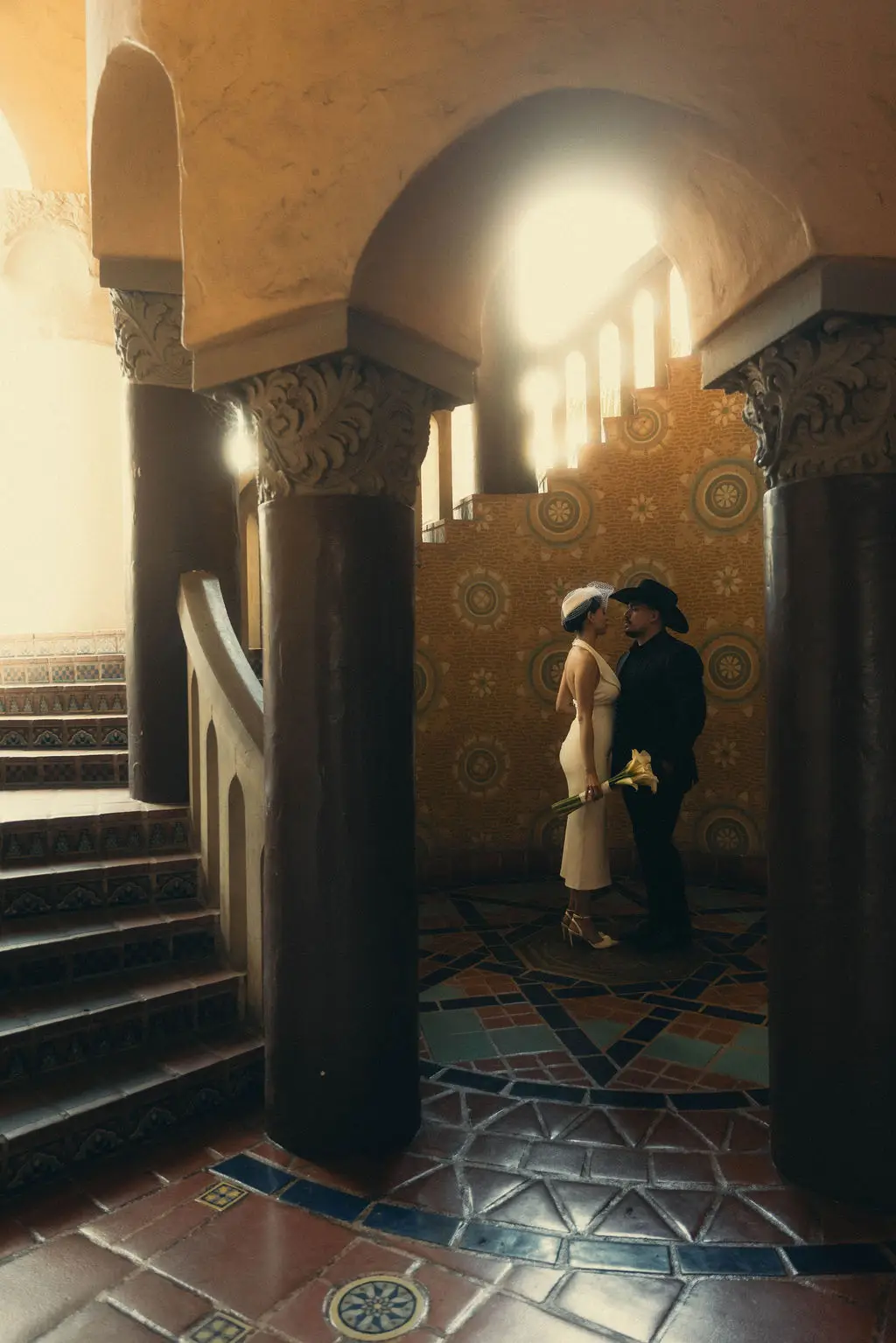 Bride and groom embrace in a tiled Moorish alcove with columns and patterned floor in warm light