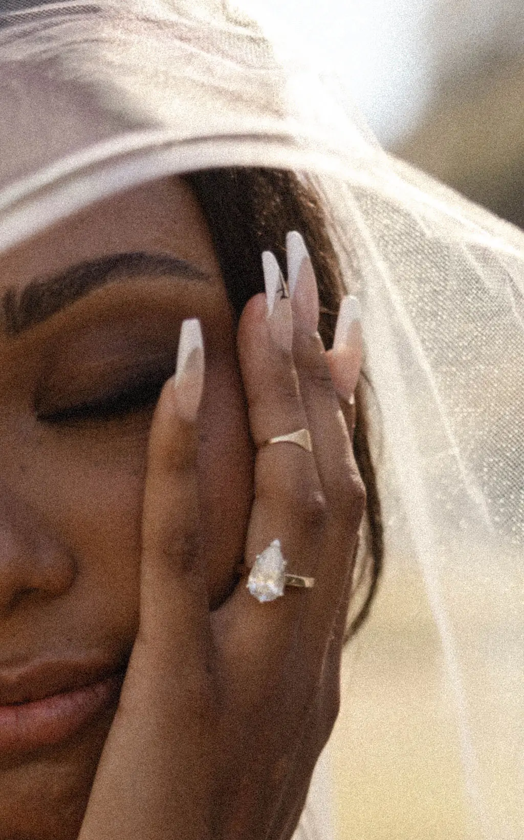 Close portrait of a bride under a veil resting her hand on her face, showing a pear diamond ring