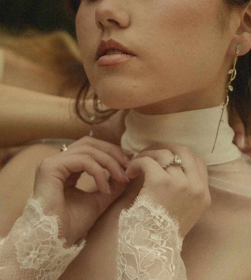 Close editorial detail of a bride's hands at her high lace collar with drop earring and ring