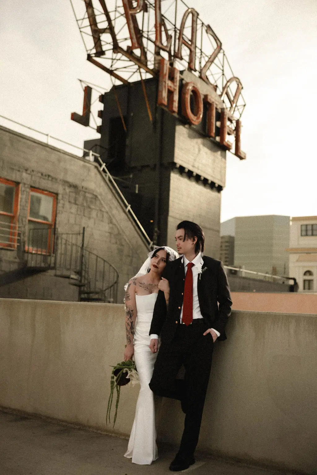 Bride and groom lean together on a rooftop beneath a vintage Plaza Hotel neon sign at dusk.
