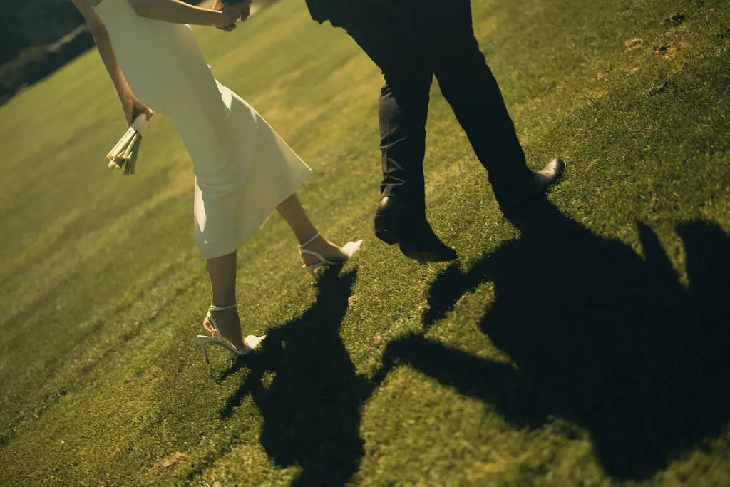 Cropped view of a couple walking across sunlit grass casting long shadows behind them