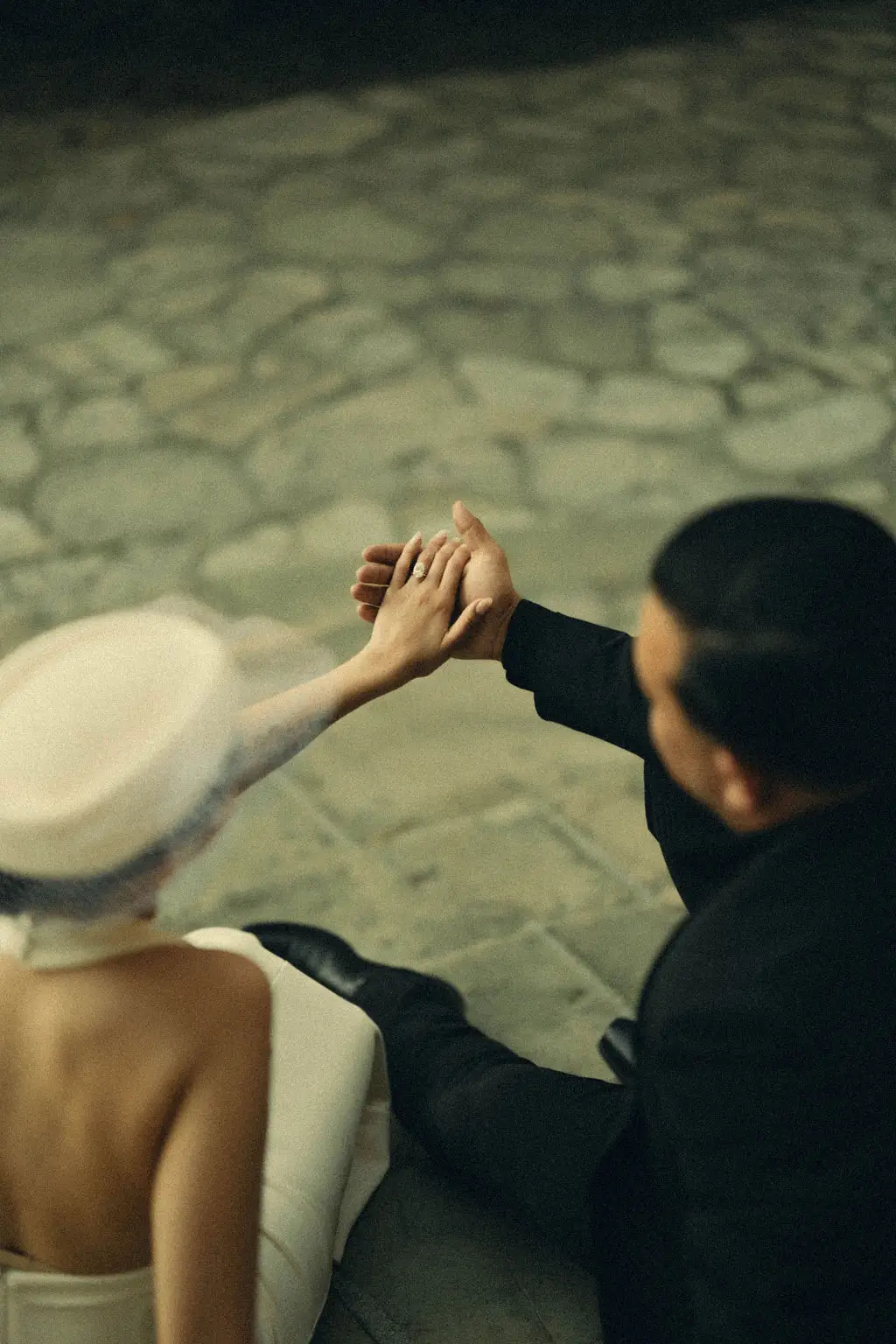 Overhead view of a couple's clasped hands as they sit together on a stone-paved courtyard
