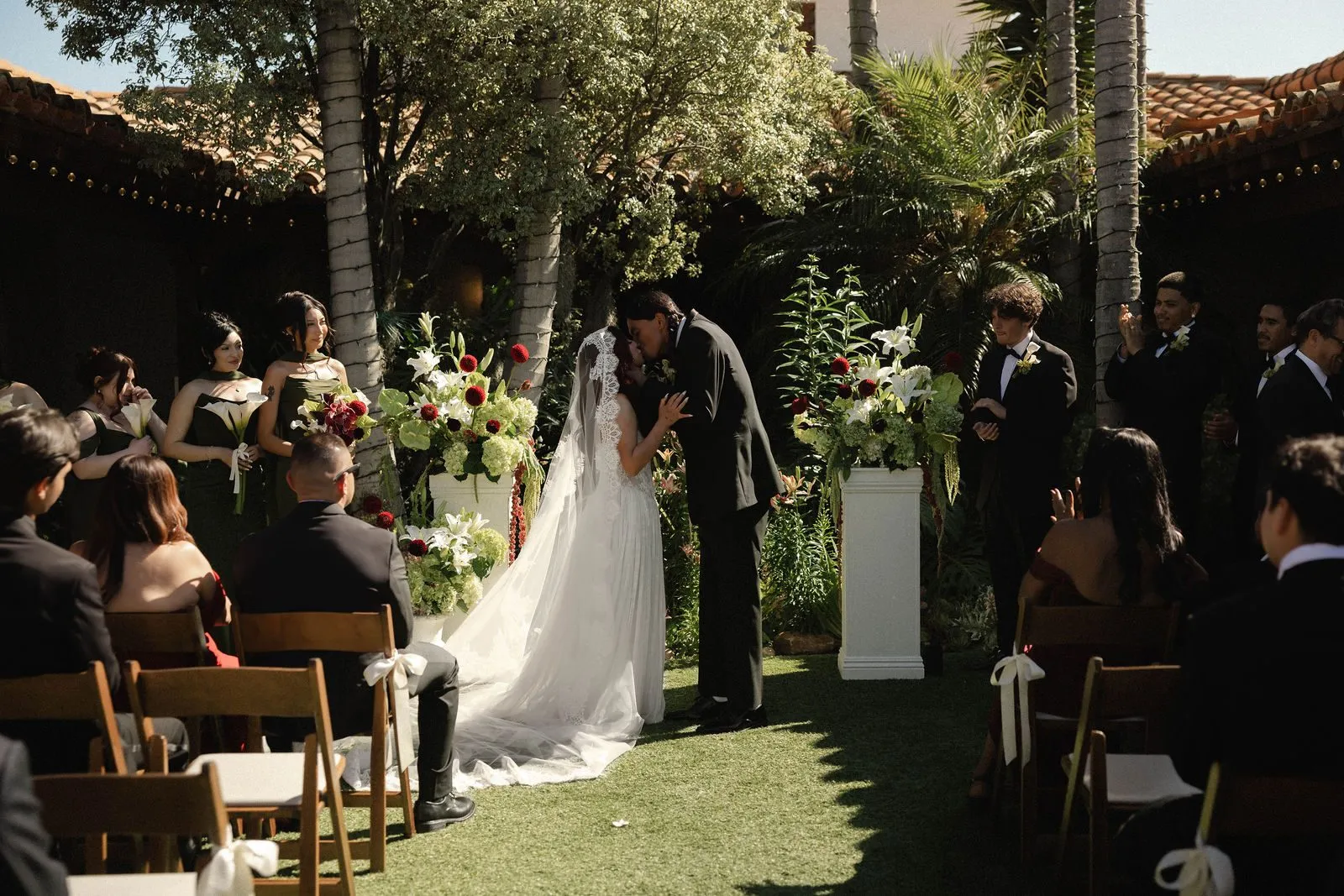 Wedding ceremony in the garden courtyard at Casa Romantica in San Clemente, with guests seated on the lawn beneath palm trees.