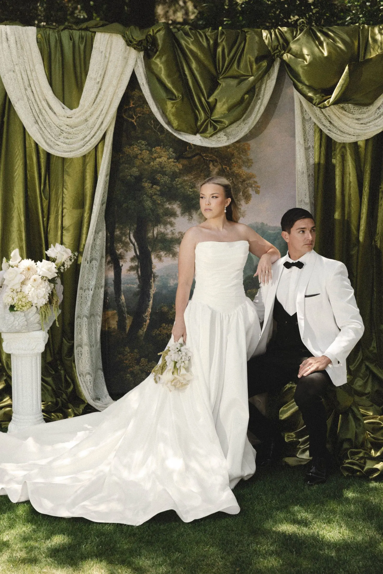 Bride with a long flowing train and groom in a tuxedo beneath an olive-draped wedding arch at Havens Country Club in Vista, California.