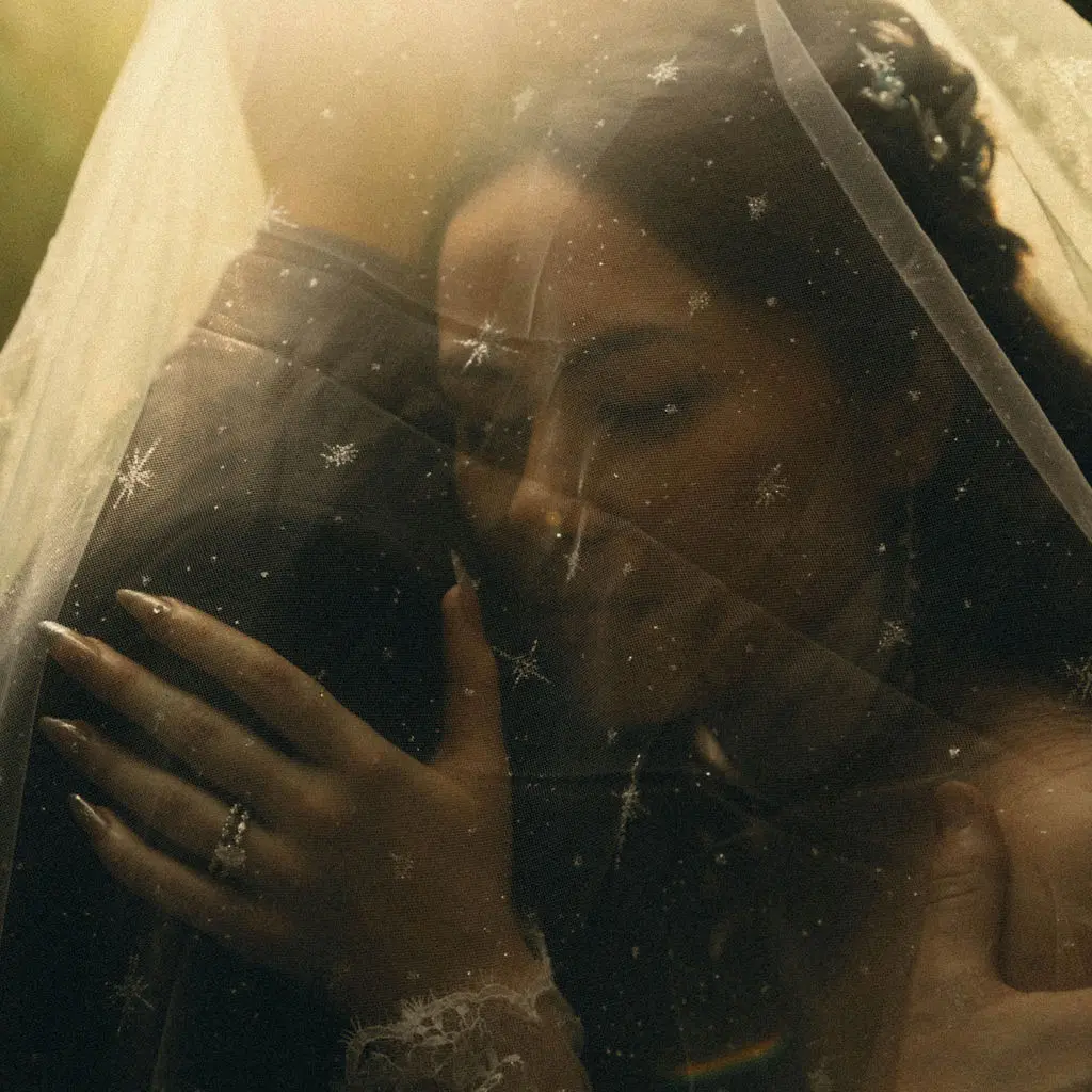 Bride with closed eyes rests beneath a star-embroidered veil showing her ring in golden light.