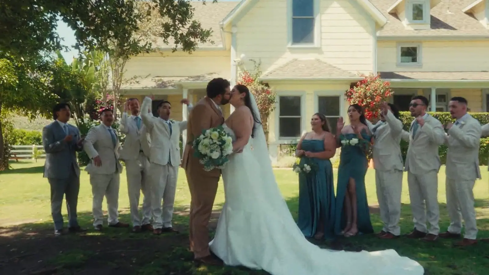 Bride and groom kiss in front of the historic ranch house at Rancho Guejito while their wedding party celebrates around them.